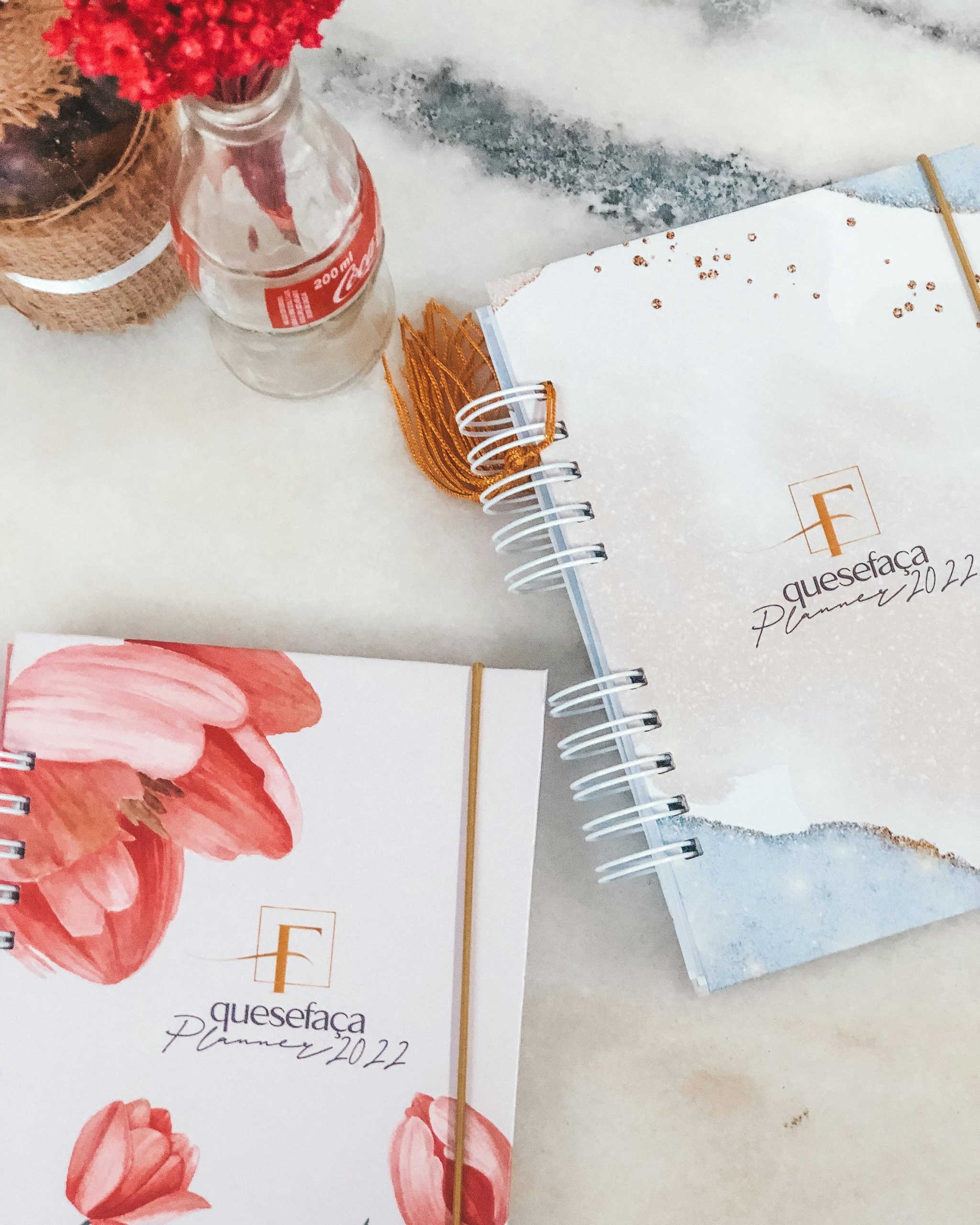 Flat lay of trendy 2022 planners with floral designs and a Coca-Cola bottle on a marble background.