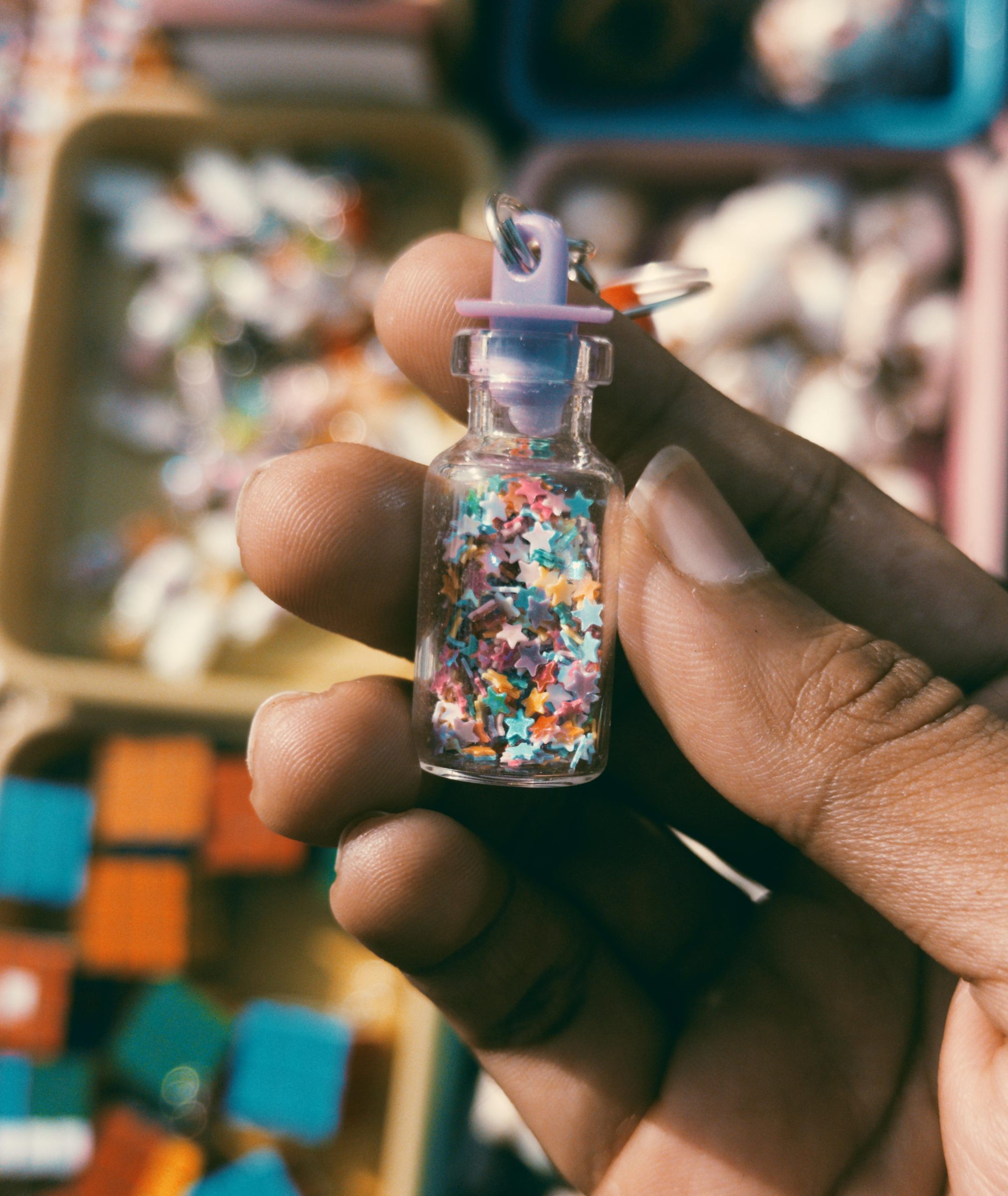 Close-up of a hand holding a tiny glass vial filled with colorful stars, perfect for creative projects.